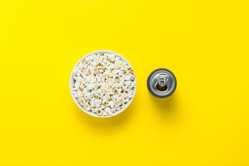 Bowl with popcorn and a can with a drink on a yellow background. The concept of watching movies and favorite TV shows, sports competitions. Flat lay, top view.