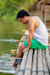 A Thai man in white tank top sitting on the bamboo raft