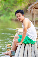 A Thai man in white tank top sitting on the bamboo raft