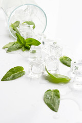 Spilled Glass with refreshing water, mint leaves and ice cubes on a light background