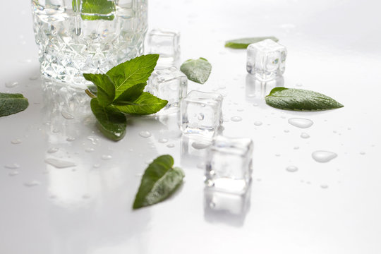 Glass with refreshing water, mint leaves, water droplets and ice cubes on a light background