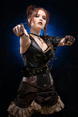 Beautiful redhead cosplayer girl wearing a Victorian-style steampunk costume with a big breast in a deep neckline points with both hands on a black and blue background.