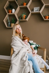 Mother and her pretty redhead daughter sit in the armchair, hugs, having fun at home.