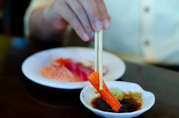 Man holding chopsticks eating fresh salmon sashimi on white  dish. Japanese food in restaurant.