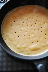 Process of baking pancakes. Delicate porous crepes on cast iron skillet. On electric induction cooker stove. Hot steam