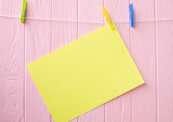 Empty sheet of orange paper on wooden background. An orange post it paper with a white paper clip isolated on wooden background