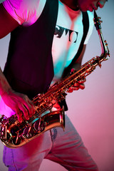 African American handsome jazz musician playing the saxophone in the studio on a neon background....