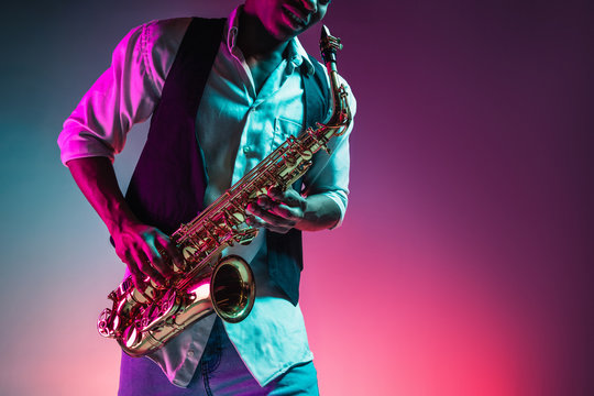 African American handsome jazz musician playing the saxophone in the studio on a neon background. Music concept. Young joyful attractive guy improvising. Close-up retro portrait.