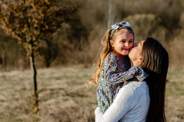 Mother holding and kissing her child outdoors on a sunny day.