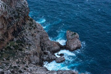 Die Wellen der rauen, blauen See schlagen weiß schäumend auf die mediterranen Felsen auf