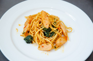 Spaghetti with sausage, Stir-fried sausage, Italian food.Spaghetti with red sauce, white plate on the table in the morning restaurant.
