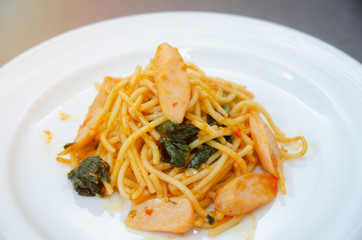 Spaghetti with sausage, Stir-fried sausage, Italian food.Spaghetti with red sauce, white plate on the table in the morning restaurant.