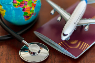 Global Healthcare and travel insurance concept. Passport Stethoscope, airplane and globe on wooden table