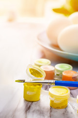 Easter concept - colorful paint with a brush and a blue plate with eggs for traditional painting eggs on a marble table on a sunny morning