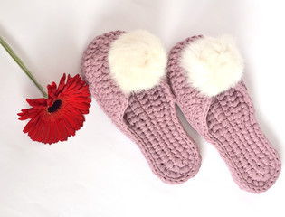 Crocheted homemade lilac slippers with fluffy white pom-poms on a white background