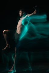 long exposure of sporty muscular mma fighter jumping in green light on black