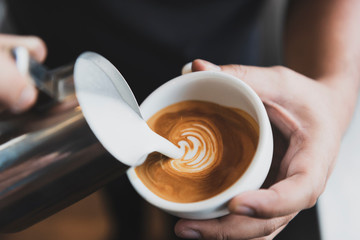 Barista making latte or Cappuccino art with frothy foam, coffee cup in cafe.