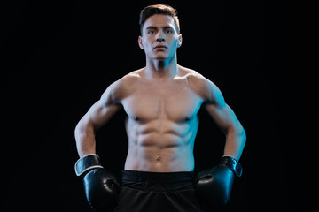 Fototapeta na wymiar confident muscular sporty boxer in boxing gloves posing isolated on black