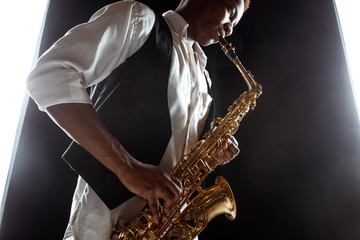 Obraz na płótnie Canvas African American handsome jazz musician playing the saxophone in the studio on a black background. Music concept. Young joyful attractive guy improvising. Close-up retro portrait.