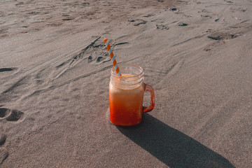 Mango smoothie in orange glass jar with paper straw on the beach