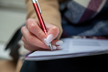 An image of a hand and pen completing a form. Woman hands with pastel manicure with pen.