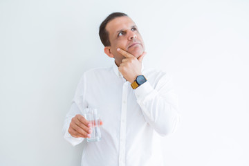 Middle age man drinking a glass of water over white background serious face thinking about...