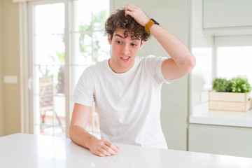 Young handsome man wearing white t-shirt at home confuse and wonder about question. Uncertain with doubt, thinking with hand on head. Pensive concept.