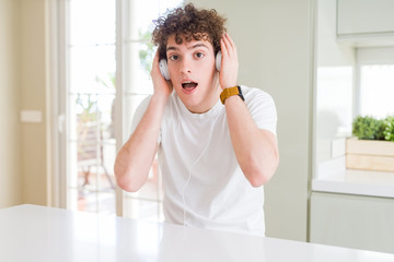 Young man listening to music wearing headphones at homes afraid and shocked with surprise expression, fear and excited face.