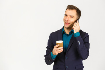 Portrait of a smiling young business man using smartphone and holding cup of coffee isolated on a white background