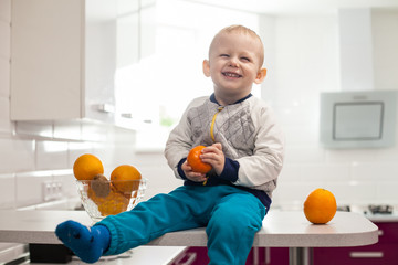 Cute toddler with fruits in kitchen.