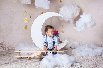 Dark-skinned little boy in a blue shirt with suspenders near the plane with clouds. African-American playing in the children's room with an airplane. Child and preschool education. Developing games.