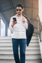 Fototapeta premium Young executive businessman using a mobile phone in the business district with skyscrapers buildings background