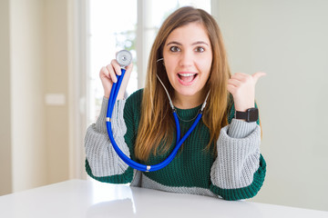 Beautiful young woman checking health with stethoscope pointing and showing with thumb up to the...