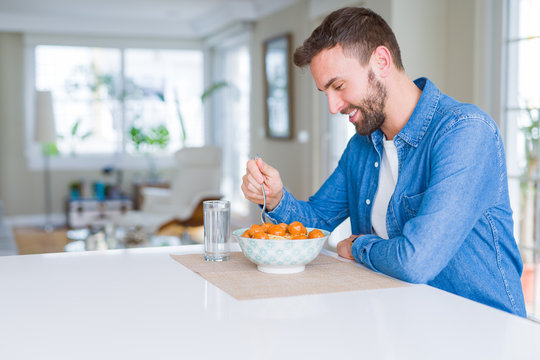 Handsome man eating pasta with meatballs and tomato sauce at home while smiling at the camera
