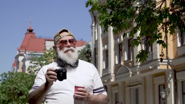 Portrait of handsome old man in cap and sunglasses take photo walking in the city