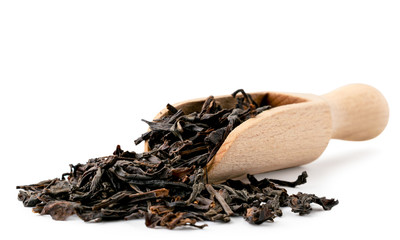 Black tea leaves spilled from a wooden spoon in close-up on a white. Isolated.