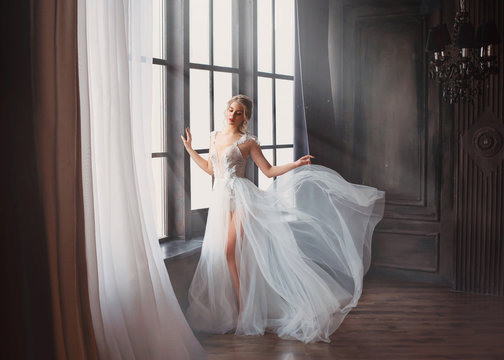 gorgeous image of graduate in 2019, girl in long white light gentle flying dress with bare leg stands alone, swan princess before performing on ballet stage, elegant lady with blond hair in sunlight