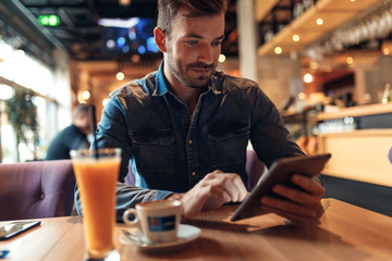 Young man sitting at cafe and looking at tablet.