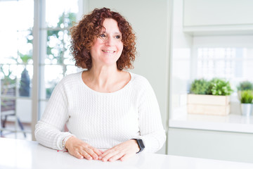 Beautiful senior woman wearing white sweater at home looking away to side with smile on face, natural expression. Laughing confident.