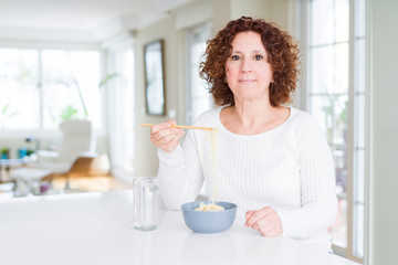Senior woman eating asian noodles using chopsticks with a confident expression on smart face thinking serious