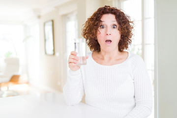 Senior woman driking a fresh glass of water scared in shock with a surprise face, afraid and excited with fear expression