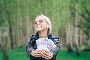 An attractive young girl with a satisfied expression boasts of his pile of bills from European Euros, walking in a green Park.