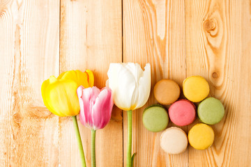 Colorful macaroons with tulips on wooden background 