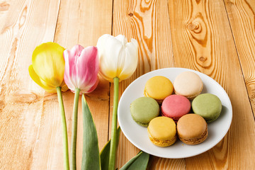 Macaroons on plate with tulips on wooden background 