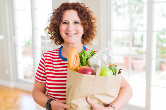 Senior woman holding paper bag full of fresh groceries from the supermarket with a happy face standing and smiling with a confident smile showing teeth