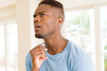 Handsome young african man thinking and questioning with pensive face, hand on chin wondering about a doubt