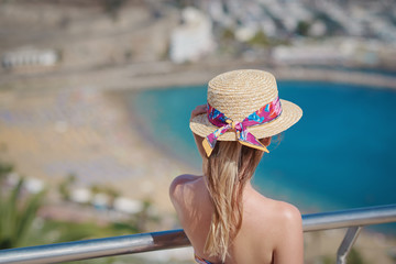 Young girl in bonnet hat is observing wonderful hotel’s view. Back view.