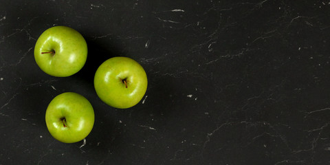 Overhead shot, three green apples on black marble like board, wide banner with space for text right.