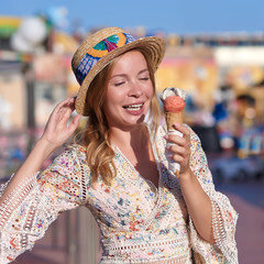 Cute European lady is walking along the amusement park and eating a strawberry ice-cream.