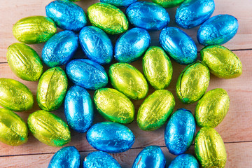Top view on variety of holiday Easter decorative eggs covered by green, blue foil laying on wooden table